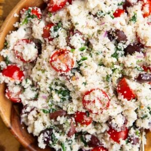 Couscous salad in a wooden bowl with a golden napkin to the side and a golden spoon for serving.
