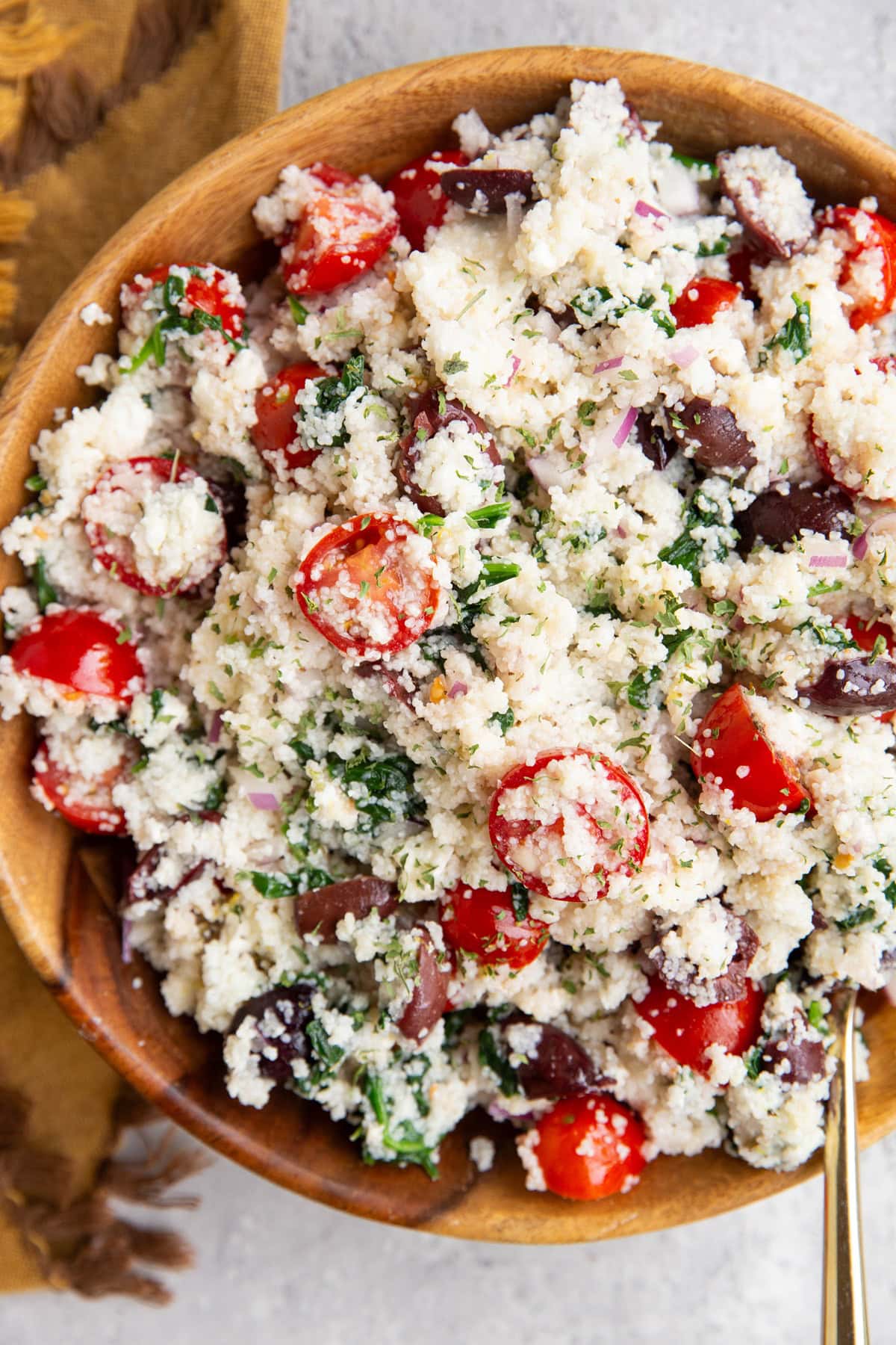 Couscous salad in a wooden bowl with a golden napkin to the side and a golden spoon for serving.