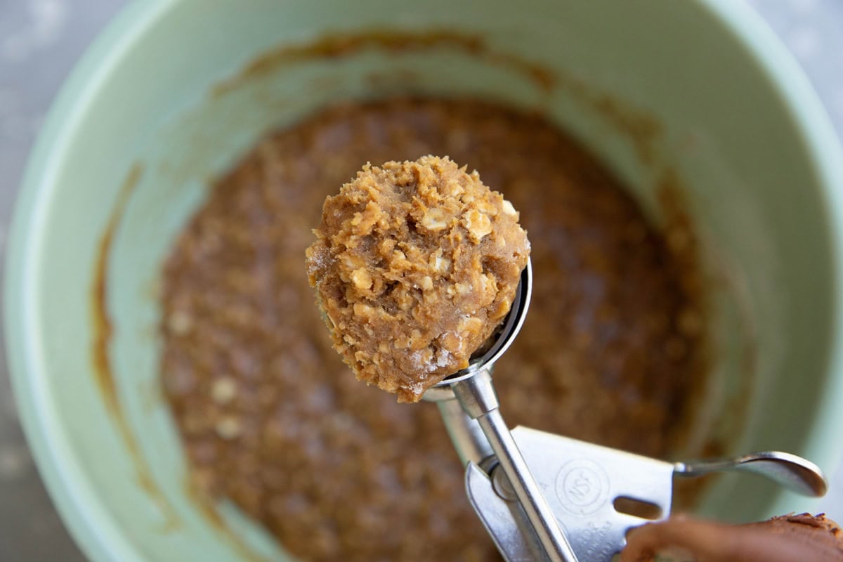 Cookie scoop scooping a mound of oatmeal cookie dough out of a mixing bowl.