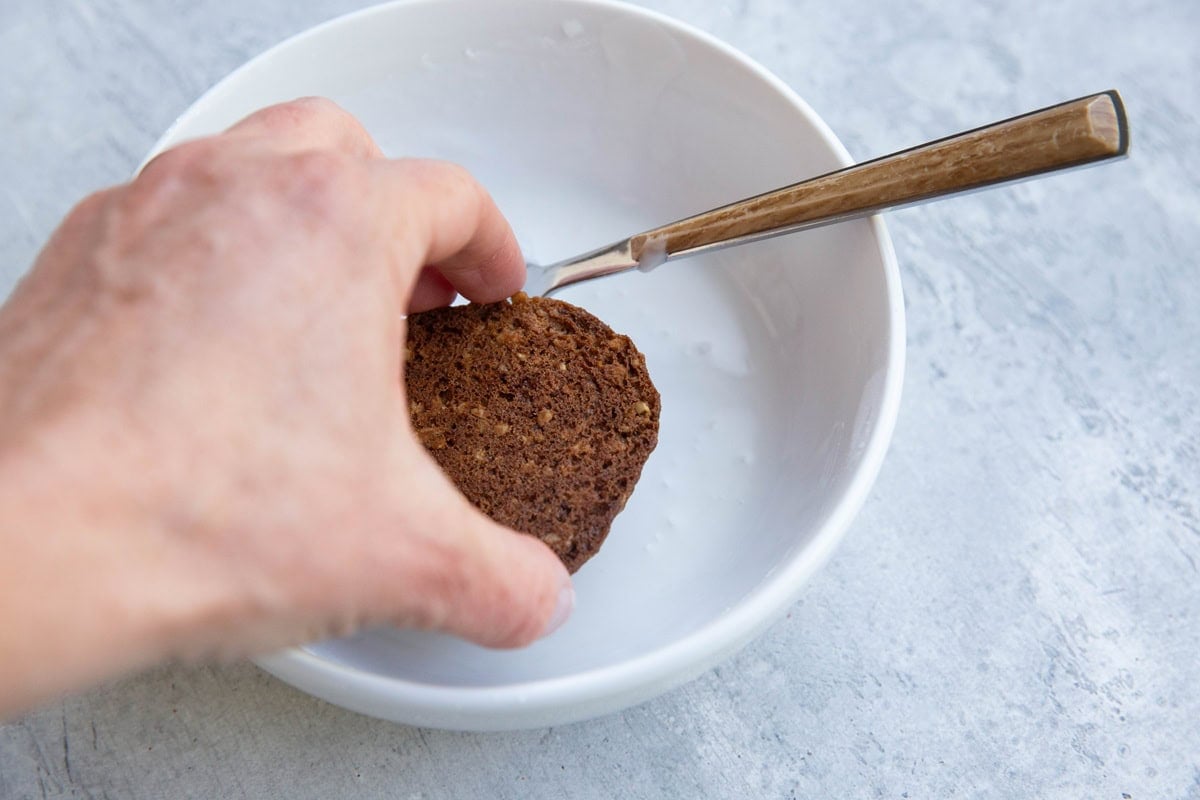 Hand dipping a cookie upside down into a bowl full of glaze to make glazed cookies.