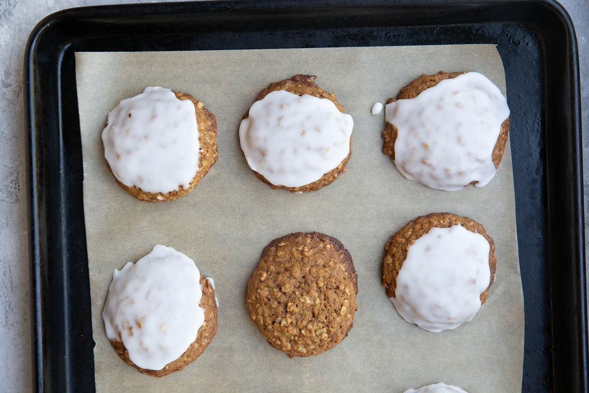 Baking sheet lined with parchment paper with iced oatmeal cookies fresh out of the oven.