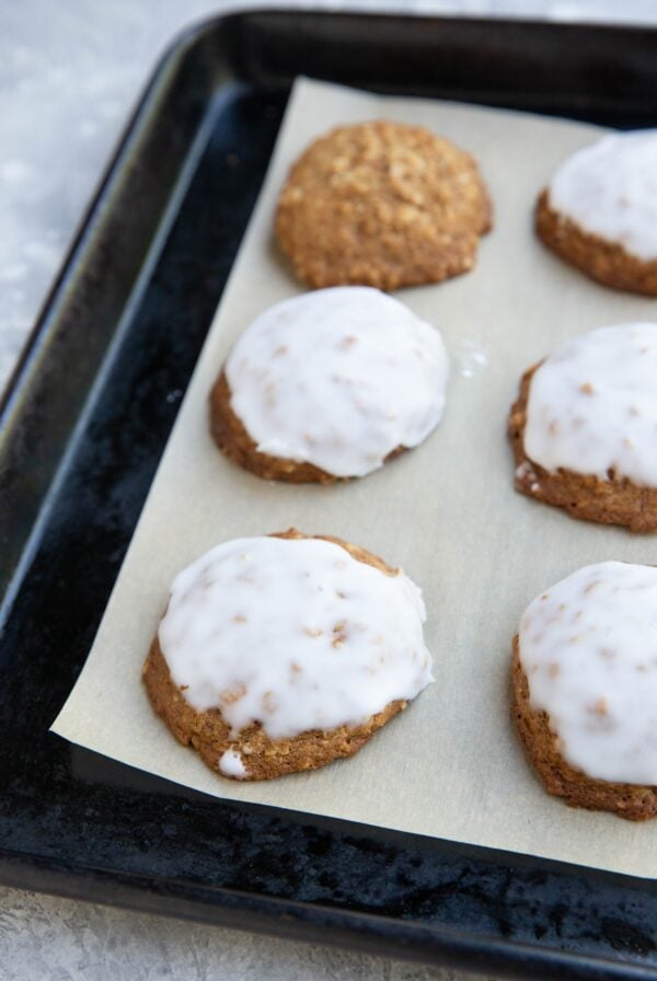 Baking sheet with iced oatmeal cookies on top of a sheet of parchment paper. Ready to serve.