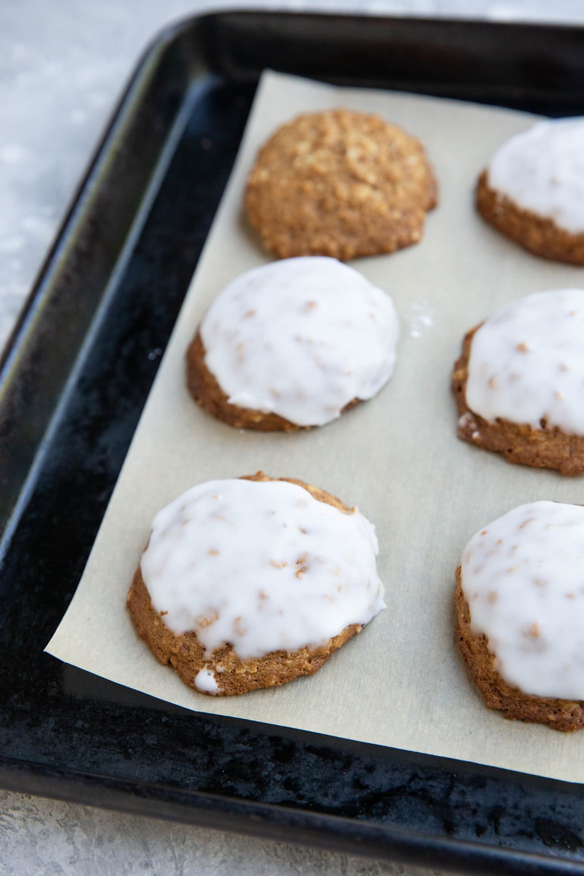 Baking sheet with iced oatmeal cookies on top of a sheet of parchment paper. Ready to serve.