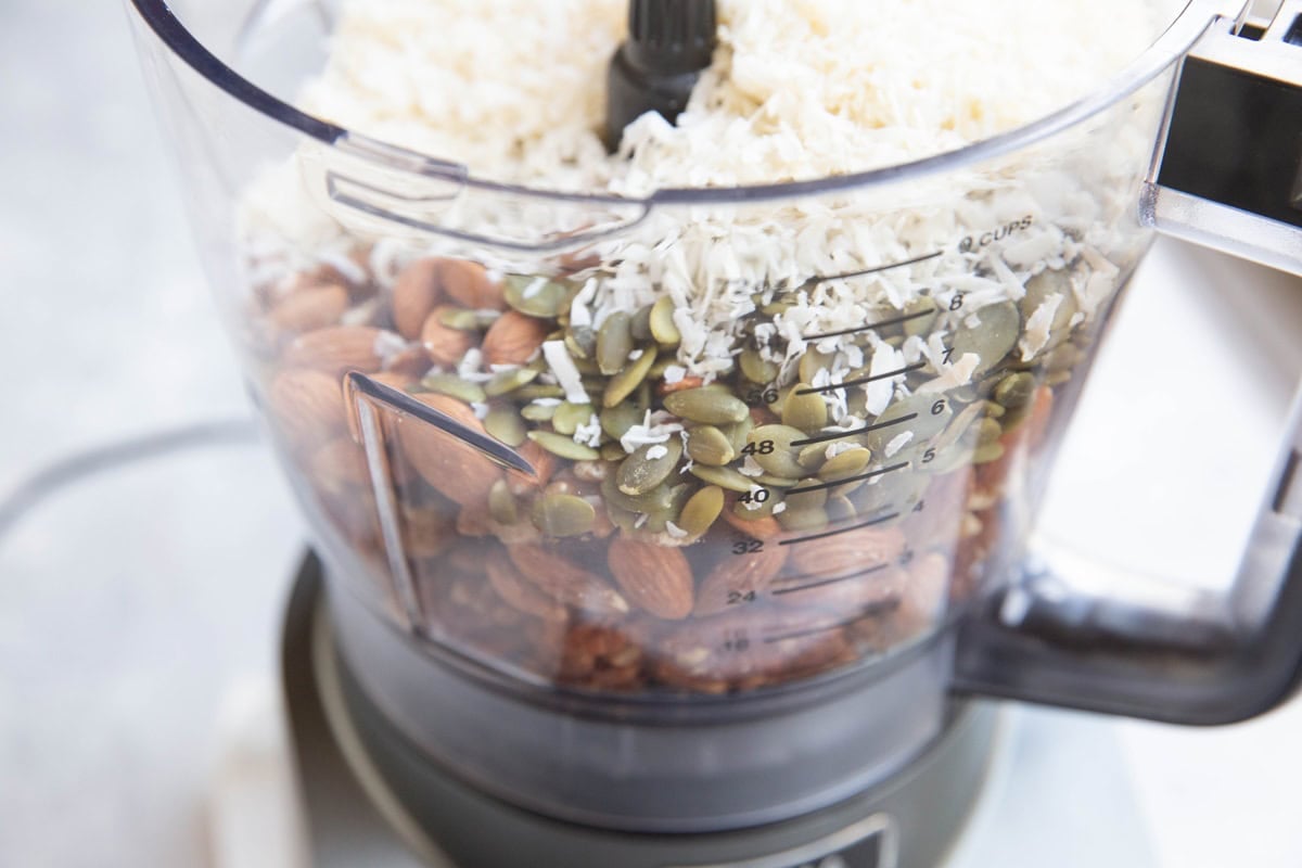 Nuts, seeds, and shredded coconut in a food processor to be processed.
