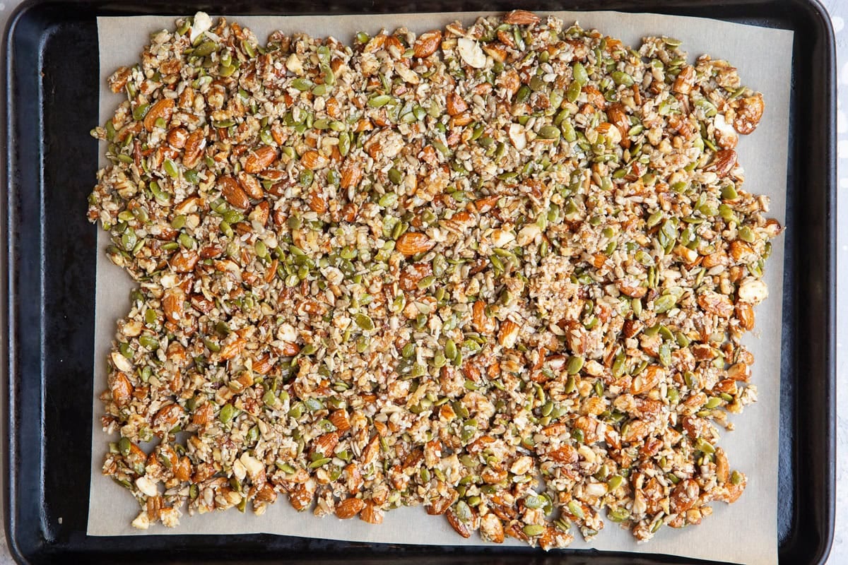 Rimmed baking sheet lined with parchment paper with granola mixture on top in a single layer.