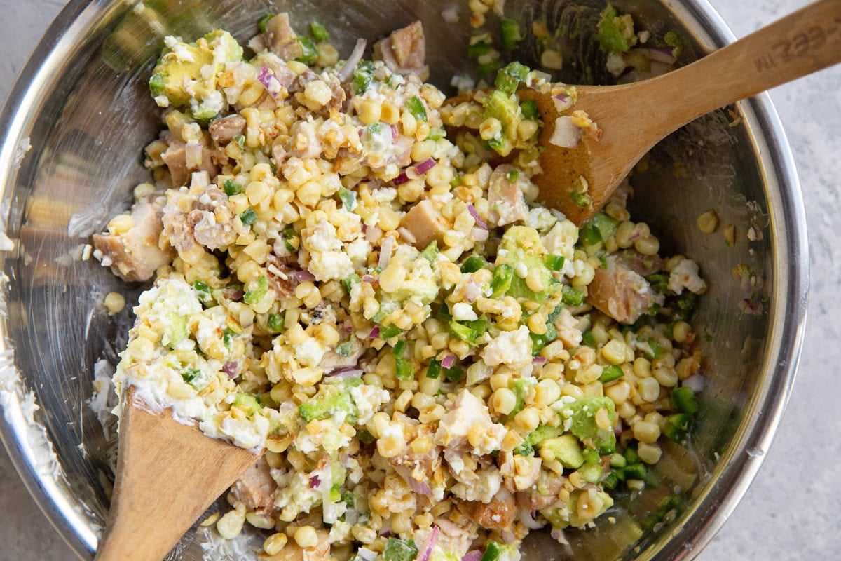Stainless steel bowl full of corn, chicken, avocado, cotija, Greek yogurt, and lime.
