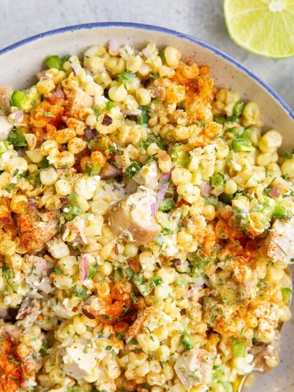 Blue rimmed bowl full of Mexican street corn salad with fresh limes to the side.