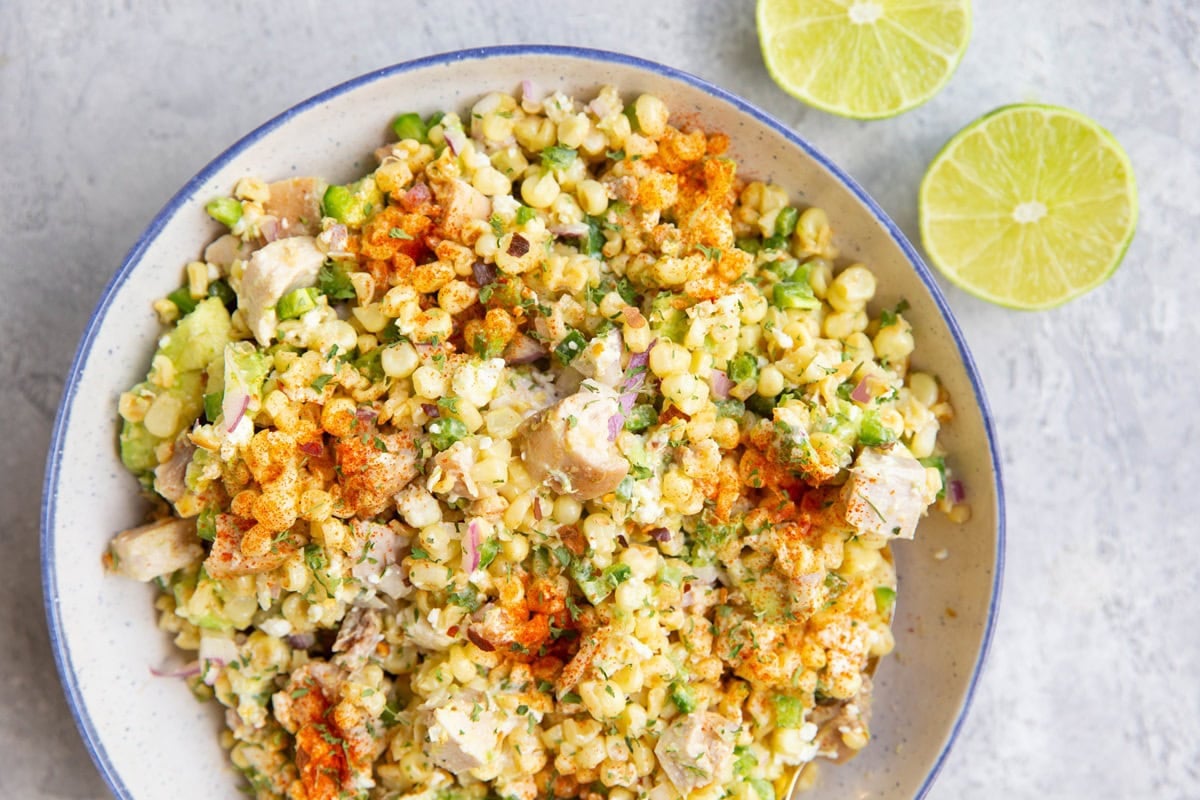 Blue rimmed bowl full of Mexican street corn salad with fresh limes to the side.