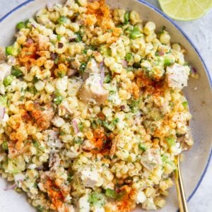 Mexican street corn salad in a blue rimmed bowl with a lime sliced in half to the side.