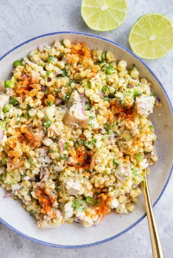Mexican street corn salad in a blue rimmed bowl with a lime sliced in half to the side.