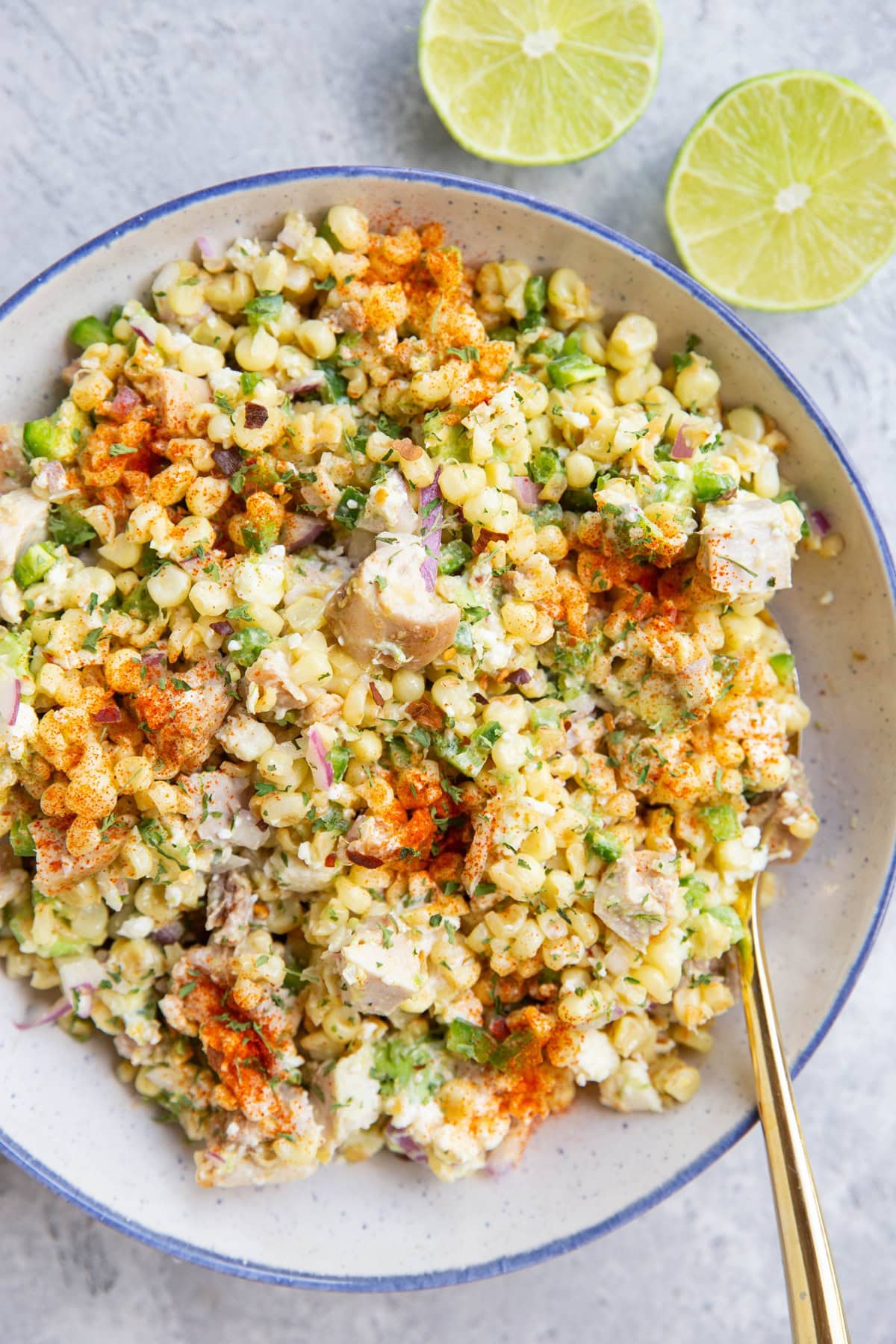 Mexican street corn salad in a blue rimmed bowl with a lime sliced in half to the side.