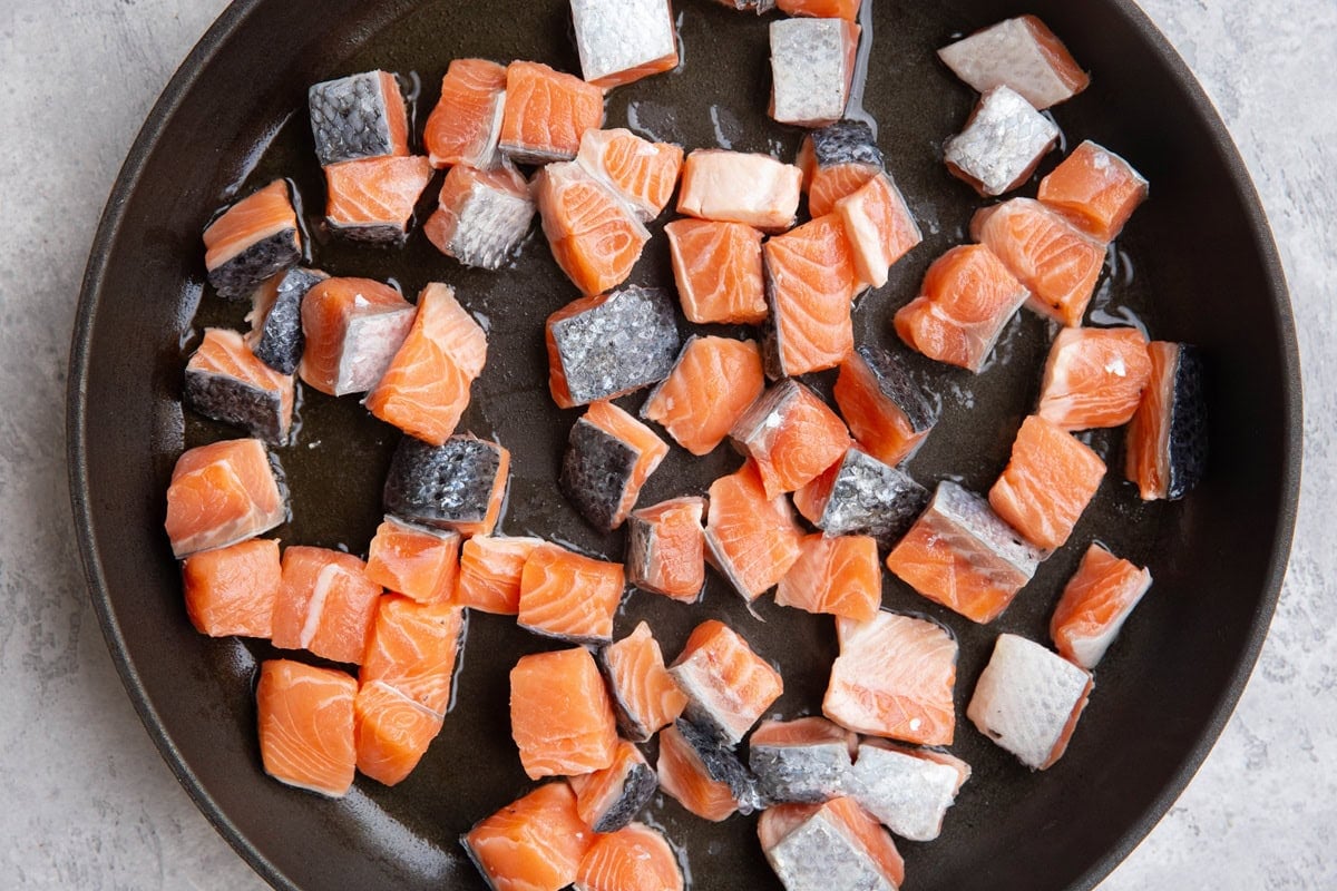 Skillet with chunks of salmon cooking in oil.