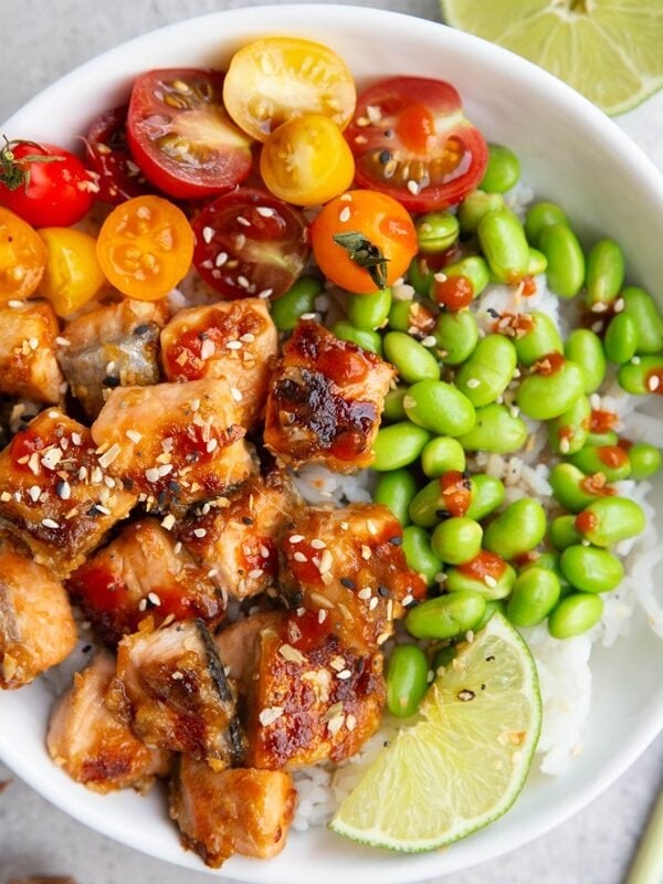 White bowl of miso salmon, edamame, and cherry tomatoes over a bed of white rice.