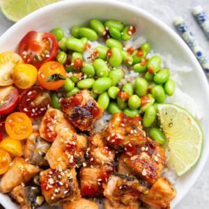 White bowl full of miso salmon, edamame, and tomatoes with chop sticks to the side and a half of a fresh lime to the side.