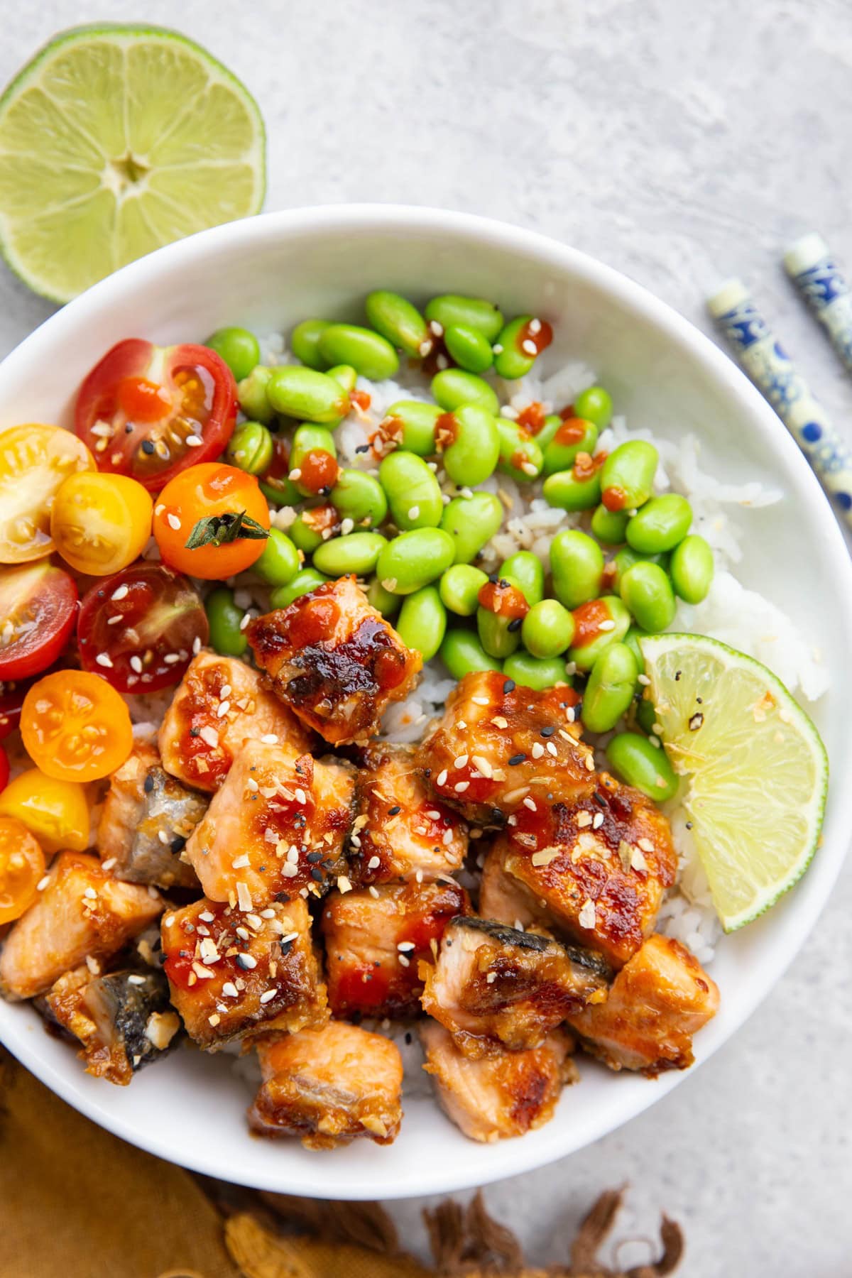 White bowl full of miso salmon, edamame, and tomatoes with chop sticks to the side and a half of a fresh lime to the side.