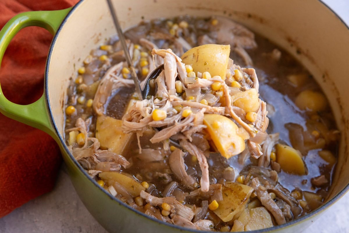 Pot of soup with shredded chicken, potatoes, corn, and broth with a ladle scooping out soup