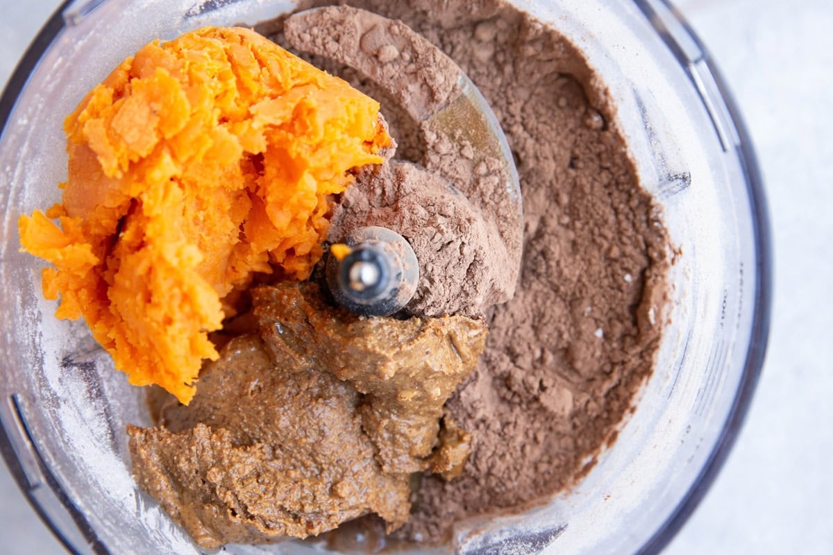 Food processor with cocoa powder, almond butter, pureed pumpkin and oats to make chocolate sweet potato oats.