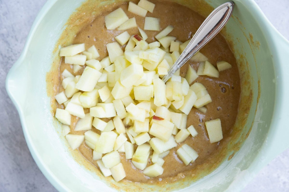 Mixing bowl with muffin batter inside and chopped apple on top, ready to be mixed in.