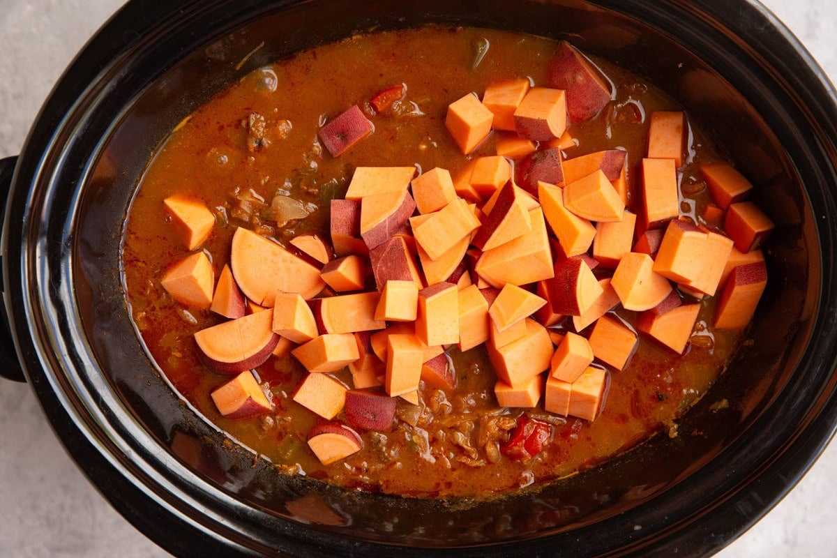 Chopped sweet potatoes on top of chili in a slow cooker to be mixed in.
