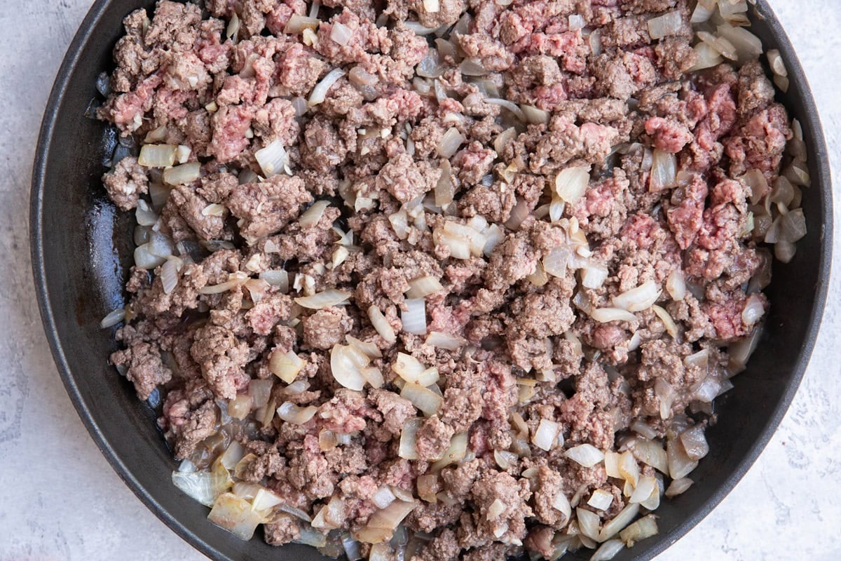 Onion and ground beef browning in a skillet to make beef chili