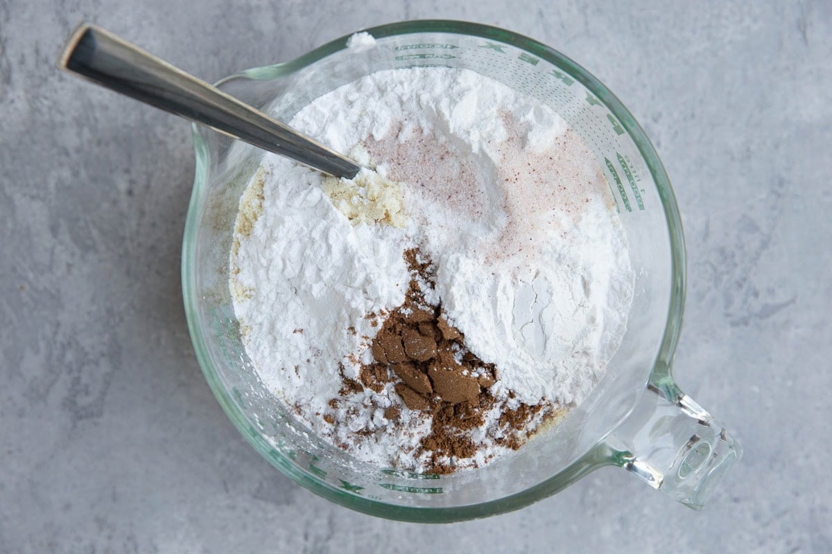 Large measuring cup with almond flour, tapioca flour, pumpkin spice, salt, and baking powder, ready to be mixed together.
