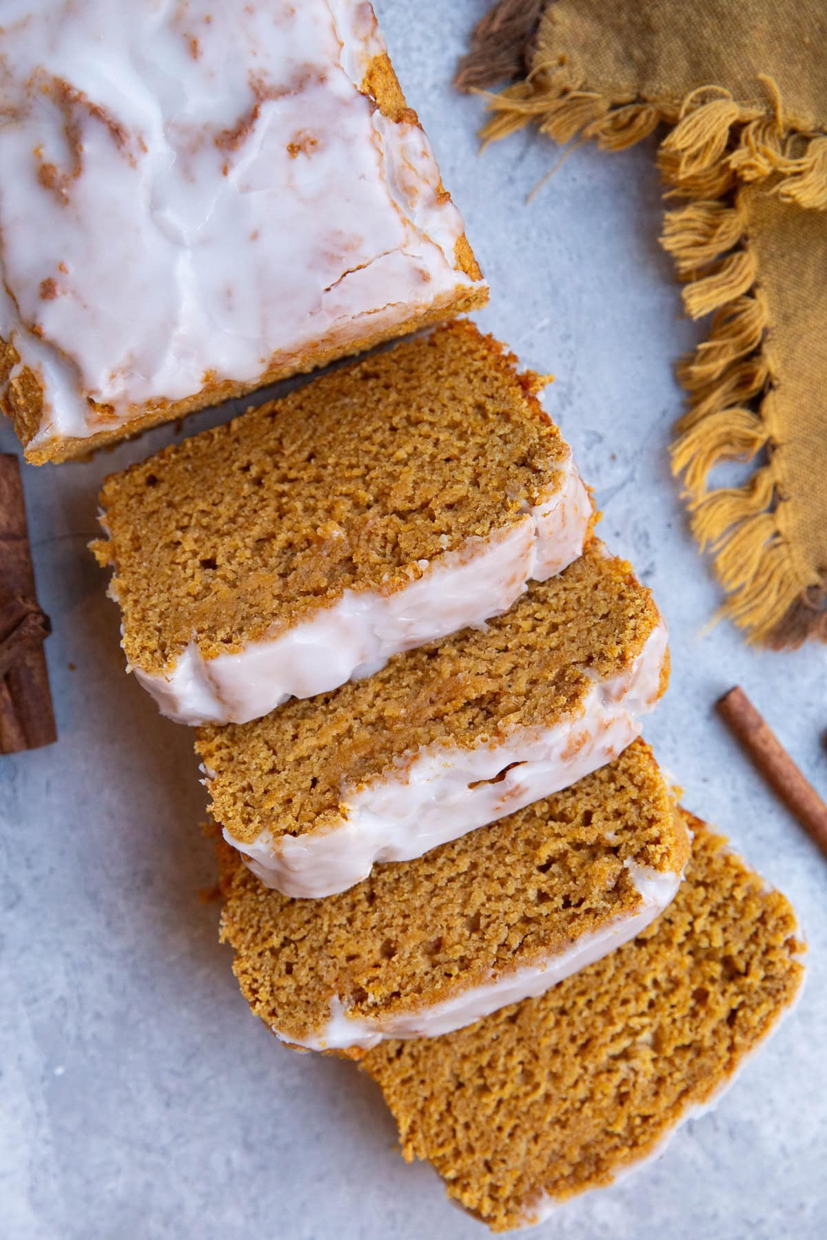 Glazed pumpkin loaf on a light blue backdrop cut into sliced with a golden napkin to the side.