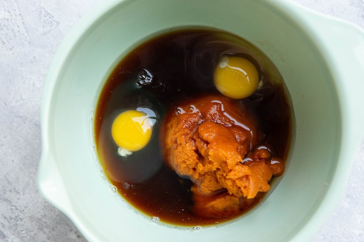 Light green mixing bowl with pureed pumpkin, eggs, and pure maple syrup inside.