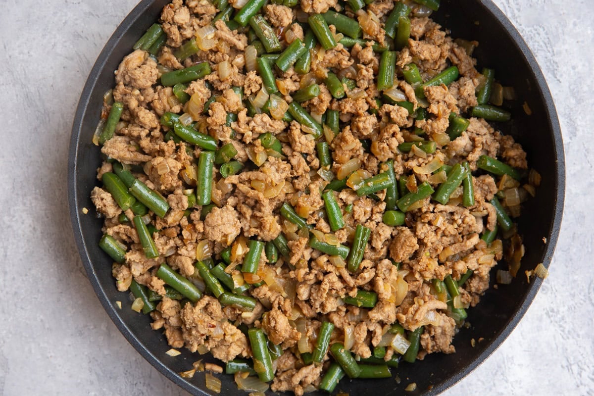 Ground beef, onion, green beans, garlic and ginger in a skillet, ready to be used.