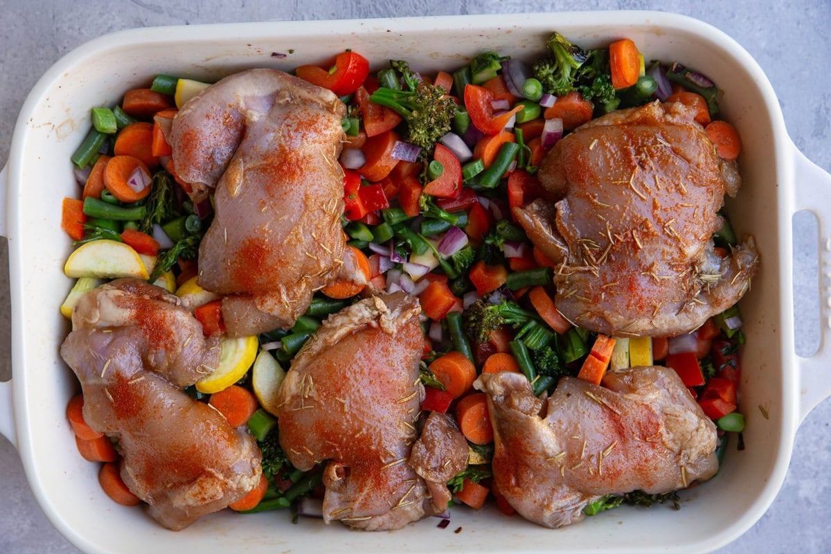 Casserole dish with chopped vegetables with marinated chicken sitting on top, ready to go into the oven.