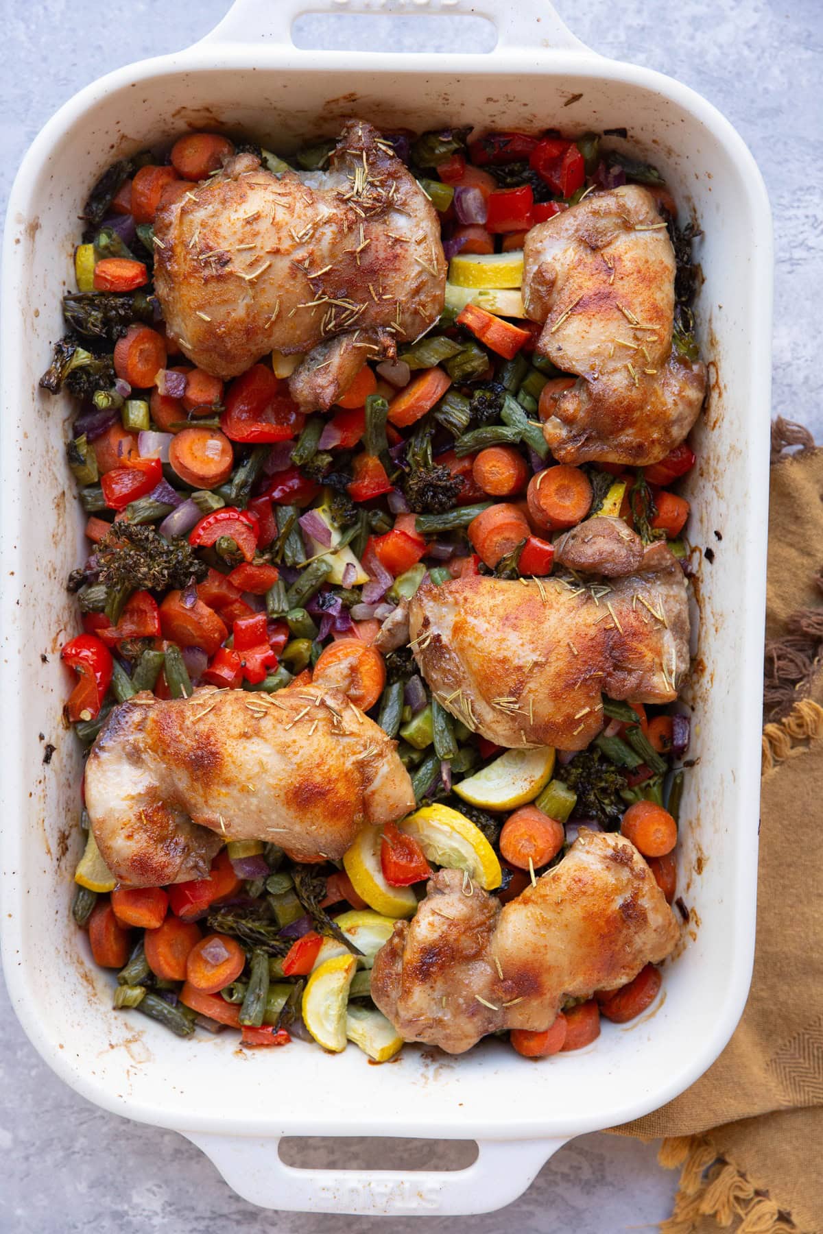 Casserole dish with chicken sitting on top of chopped roasted vegetables fresh out of the oven.