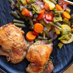Cooked chicken thighs and roasted vegetables on a black plate with a gold fork.