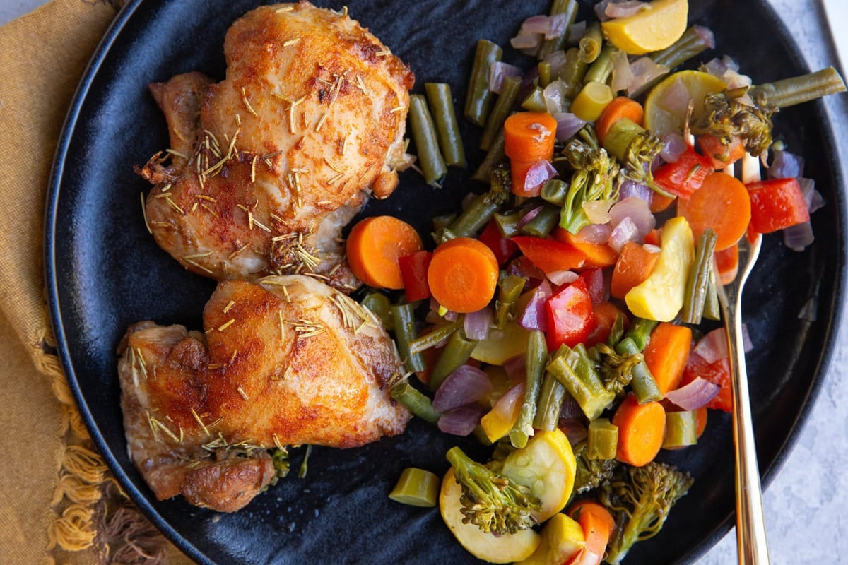 Black plate of chicken thighs and roasted veggies