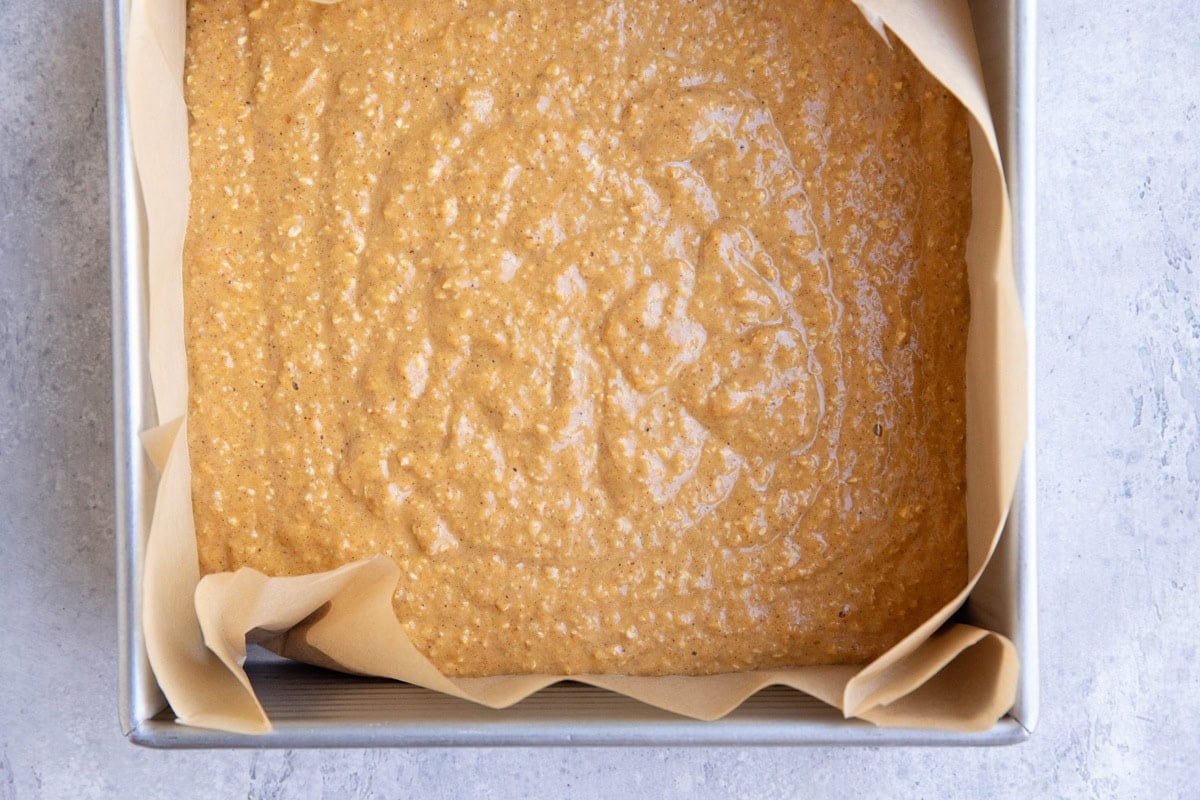 Baking pan lined with parchment paper with pumpkin cake batter inside.