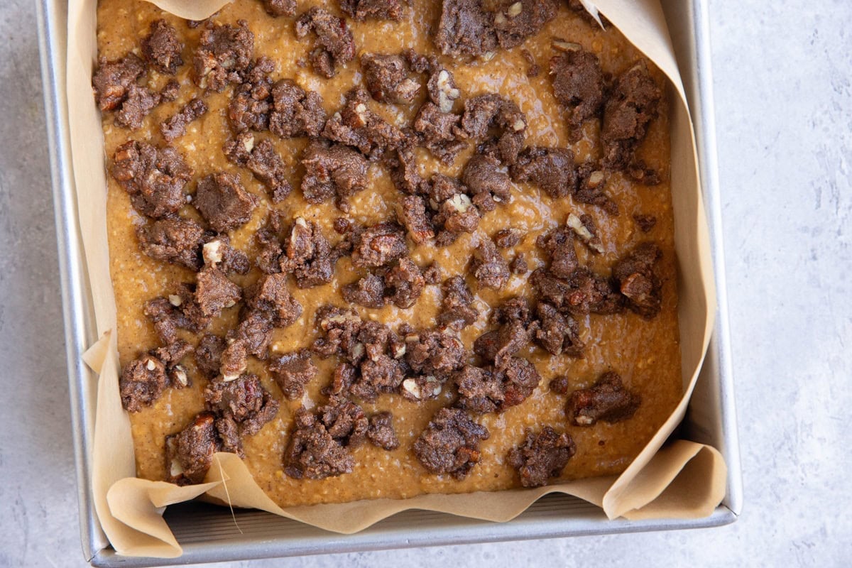 Cake pan with pumpkin cake batter inside and streusel topping mixture sprinkled on top.