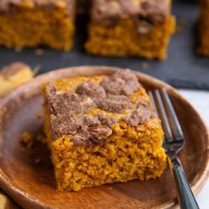 Slice of pumpkin oatmeal cake on a wooden plate with the rest of the cake cut into slices in the background on a black slate cutting board.