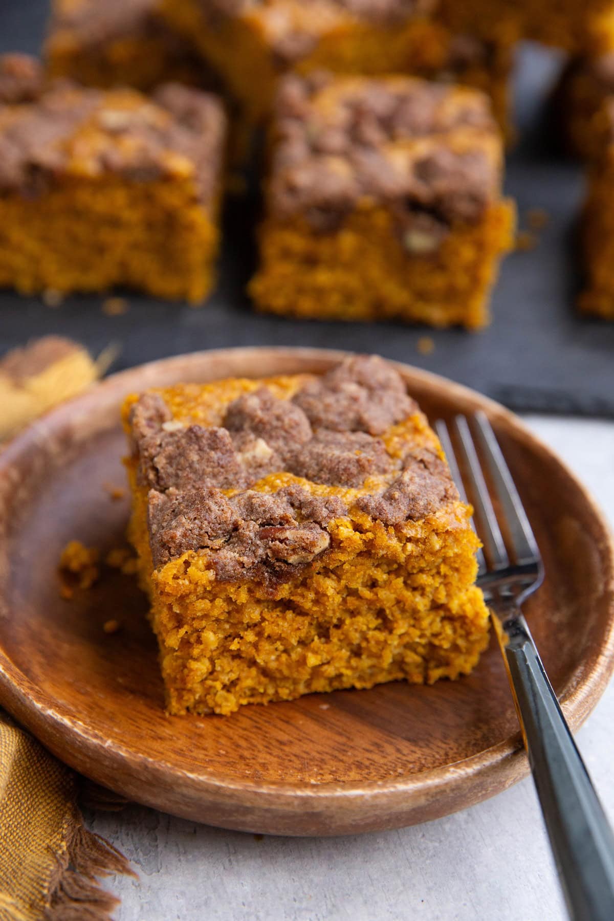 Slice of pumpkin oatmeal cake on a wooden plate with the rest of the cake cut into slices in the background on a black slate cutting board.