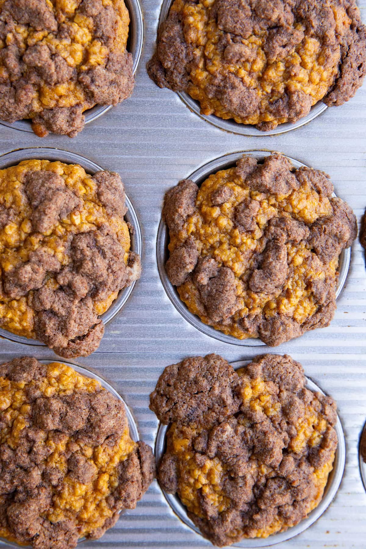 Muffin pan full of pumpkin muffins that have a crumb topping.