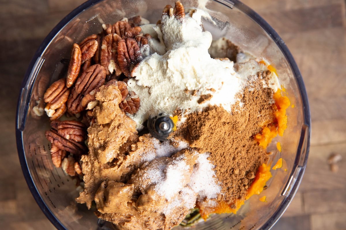 Food processor full of nuts, seeds, nut butter, protein powder, pumpkin, and pumpkin pie spice to make pumpkin protein balls.