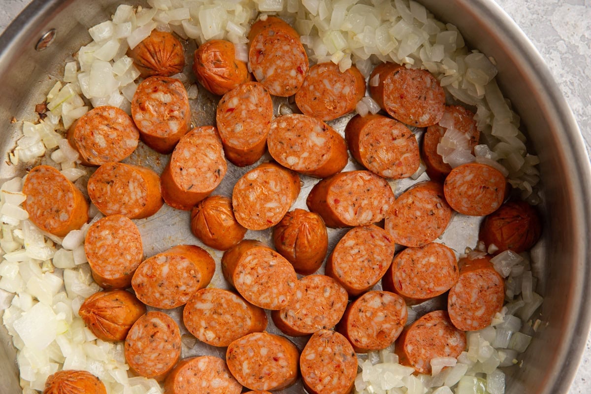 Stainless steel skillet with sauteed onion scooted off to the side and sliced sausage searing in the center.