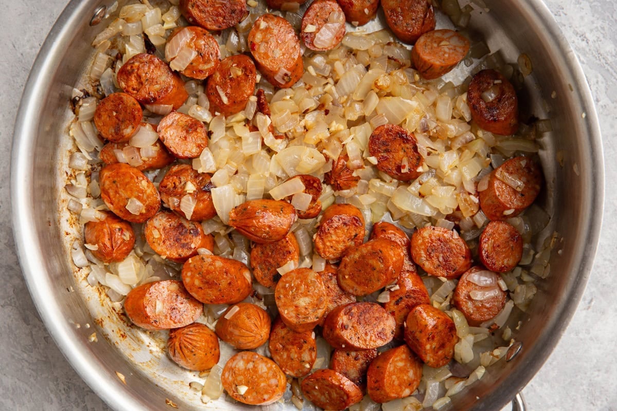 Stainless steel skillet full of sauteed onion, garlic, and sausage.