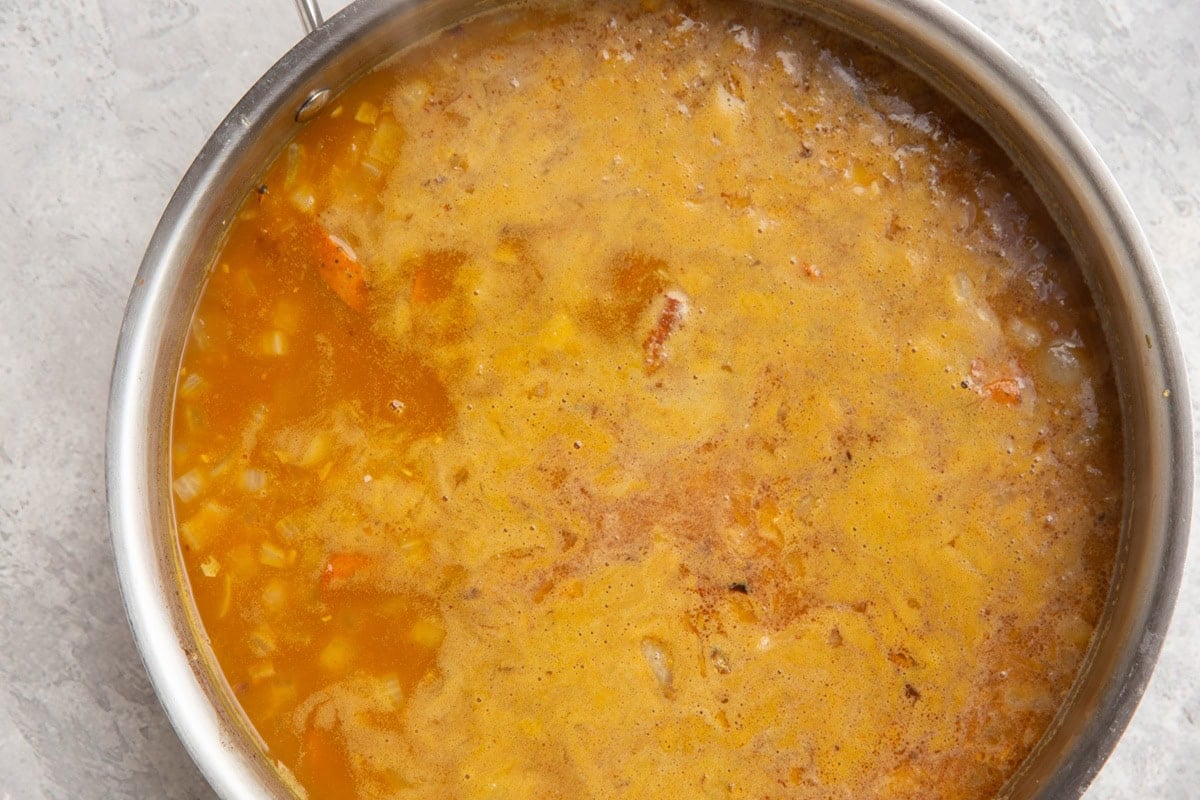 Stainless steel skillet with pumpkin, broth, onion, rice, and sausage cooking to make a one-skillet meal.