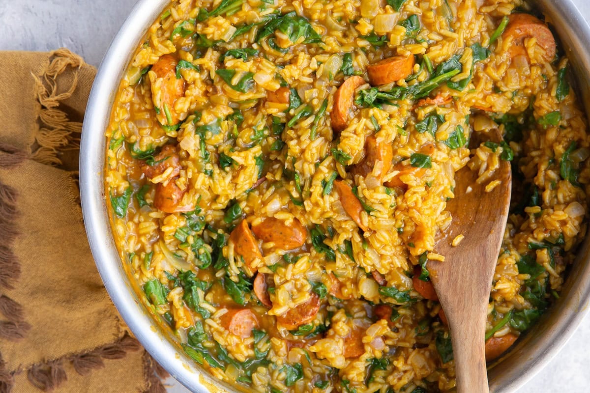 Pumpkin, sausage and rice with spinach inside of a skillet with a wooden spoon ready to serve.
