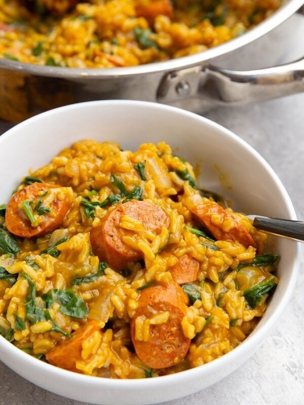 White bowl full of pumpkin rice sausage with spinach and the skillet with the rest of the meal in the background.