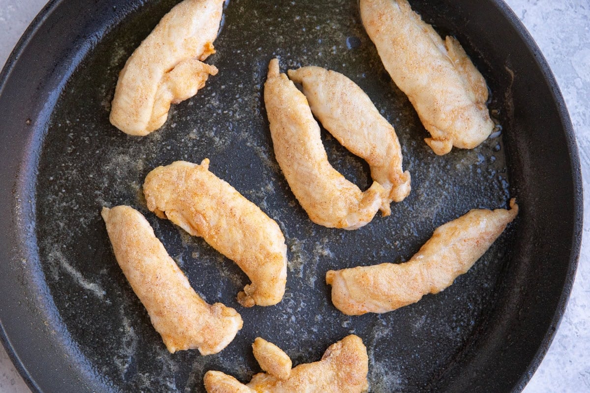 Large skillet with 8 breaded chicken tenderloins browning in a skillet.