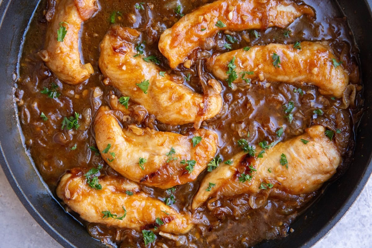 Large skillet full of golden breaded chicken cooking in a caramelized onion sauce.