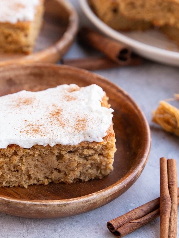 Two wooden plates with slices of spice cake with cinnamon sticks to the side and a golden napkin to the side.