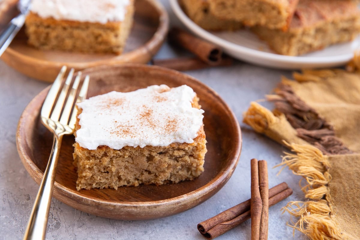 Two wooden plates with slices of spice cake with cinnamon sticks to the side and a golden napkin to the side.