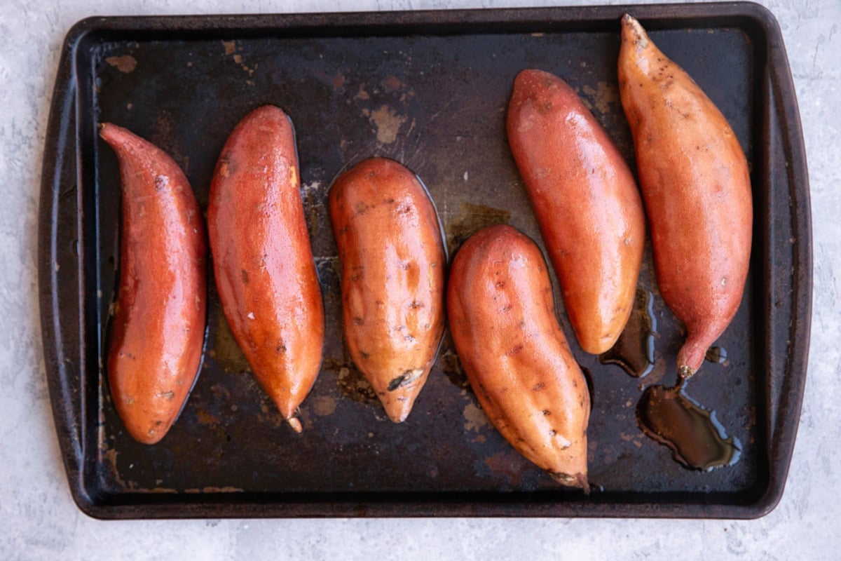 Baking sheet with six sweet potato halves cut side down drizzled in oil, ready to go into the oven.