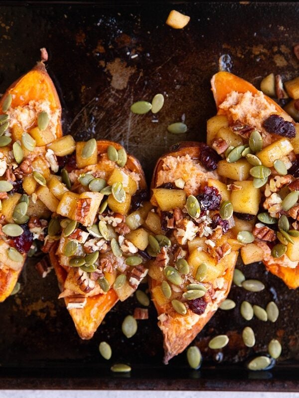 Baking sheet with sweet potato halves topped with stewed apples, dried cranberries, chopped pecans and pumpkin seeds.