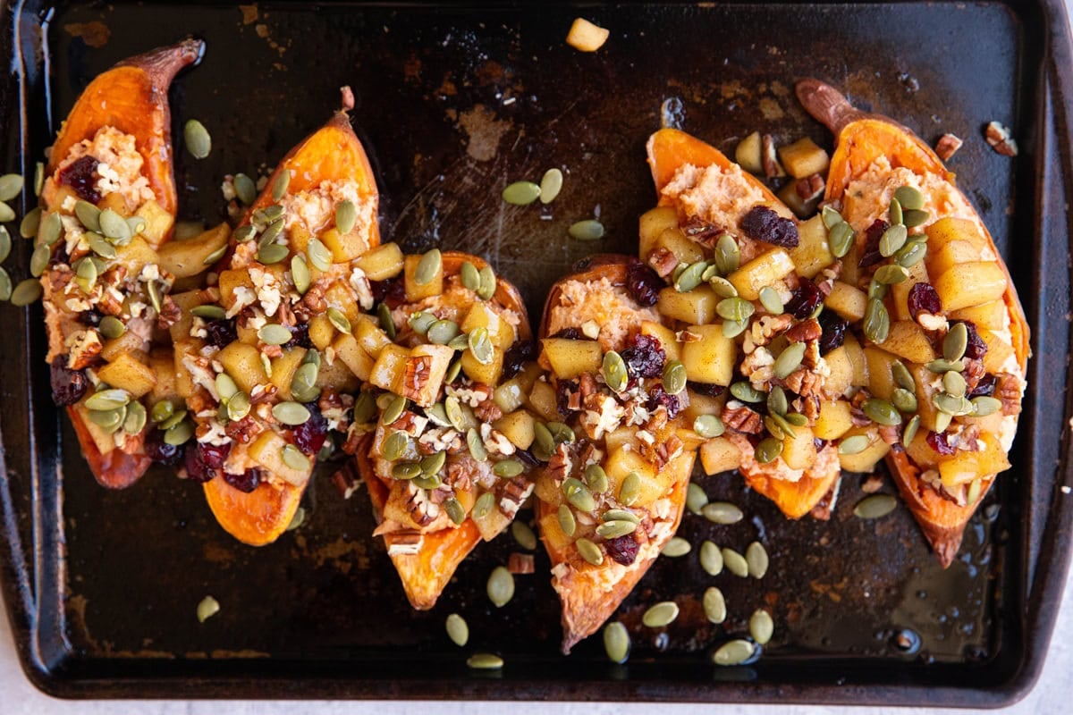 Baking sheet with sweet potato halves topped with stewed apples, dried cranberries, chopped pecans and pumpkin seeds.